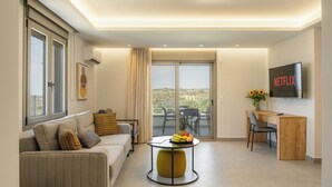 A modern living room with a sofa, a round coffee table with fruit, a desk with a chair, and a TV mounted on the wall.