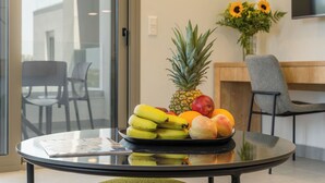 A glass table with a fruit bowl containing bananas, pineapple, and apples.
