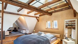 Un dormitorio con techo inclinado, vigas de madera, una cama, mesitas de noche y un espejo.