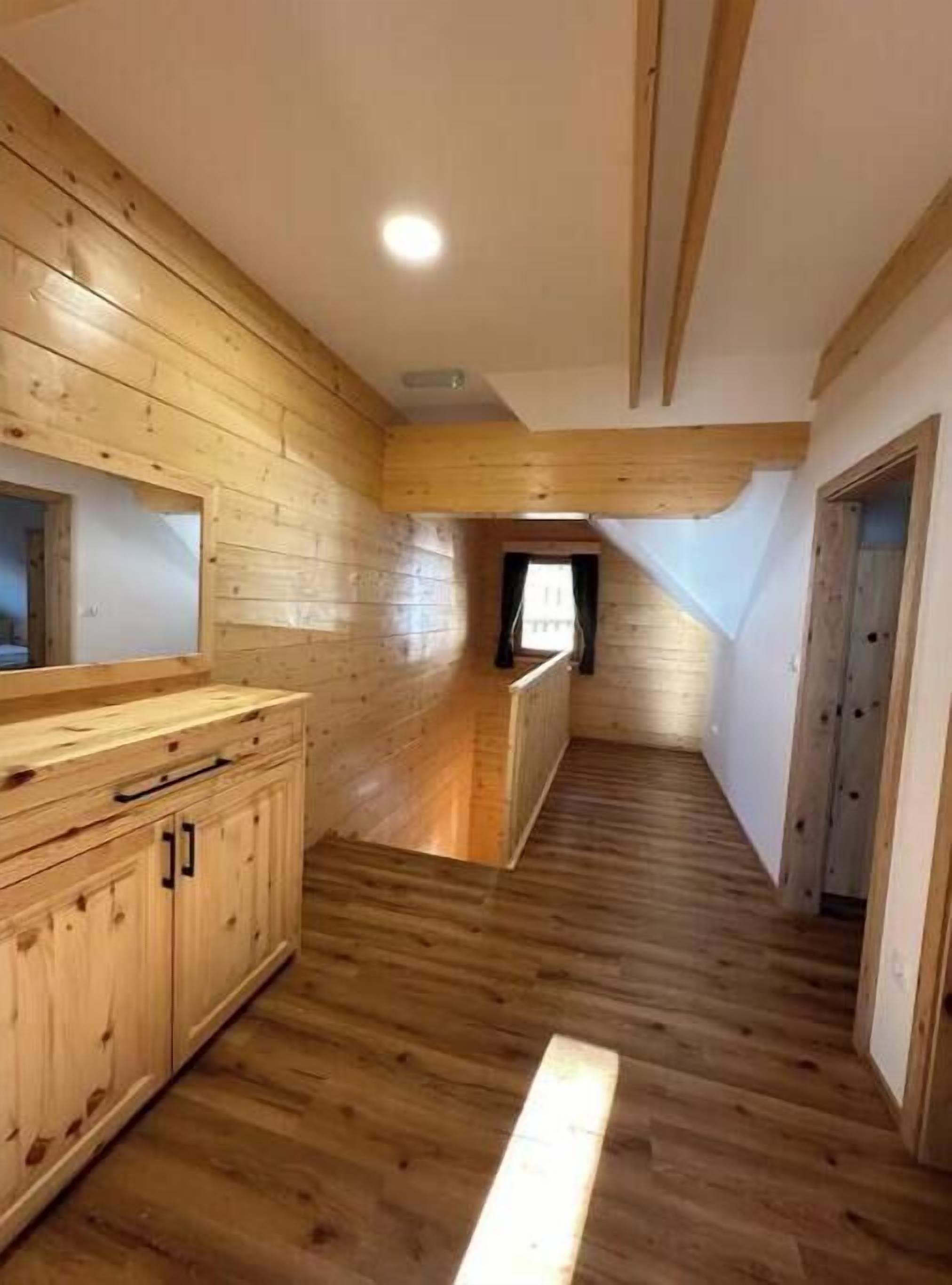 Ein schmaler Korridor mit Holzwänden und -böden, der zu einem kleinen Fenster und einer Tür führt.