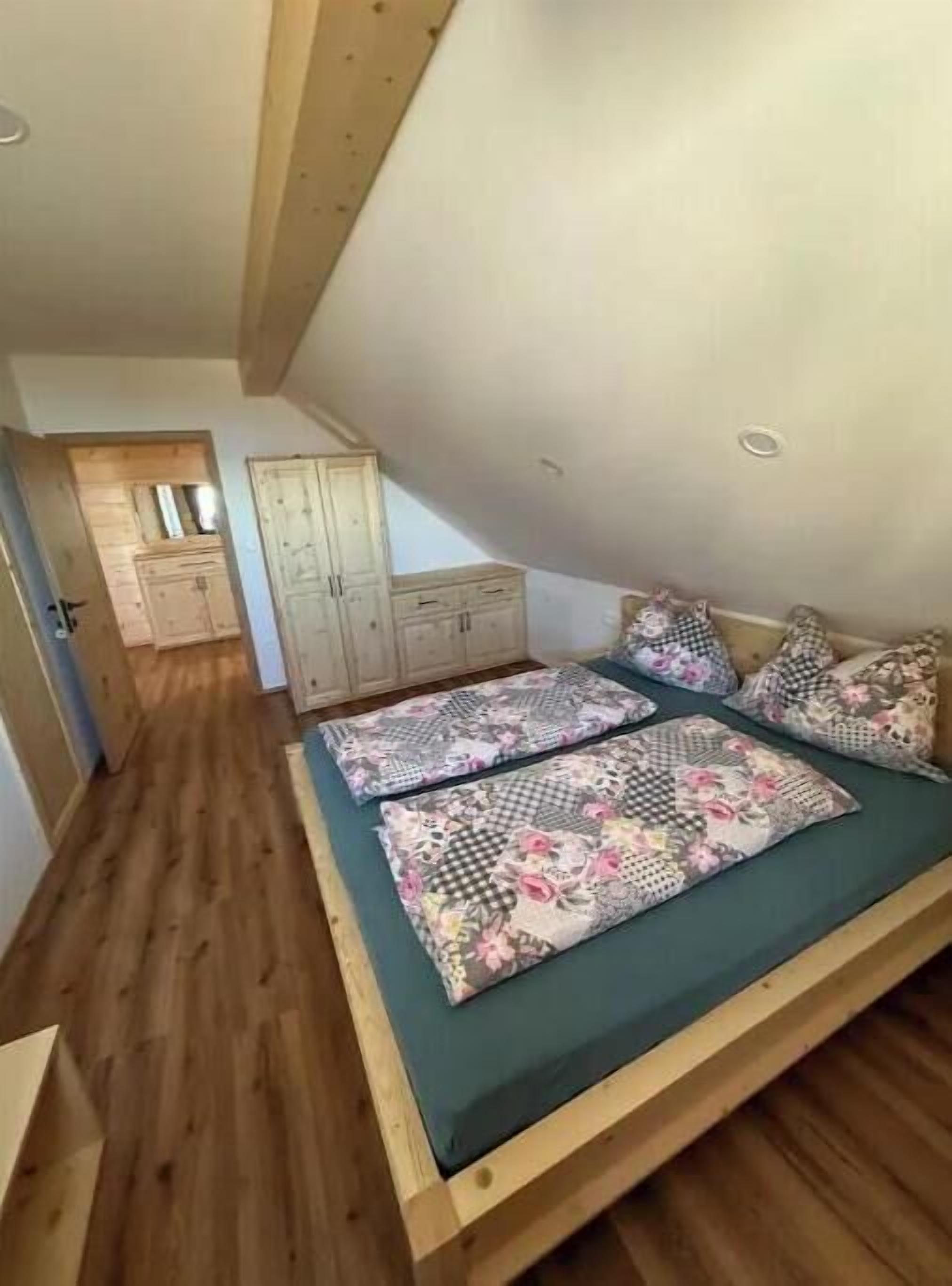 A bedroom with a sloped ceiling, wooden flooring, a bed with floral bedding, and a wardrobe.