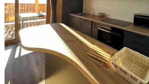 A modern kitchen with dark cabinets, a wooden countertop, and a dining area with a table and chairs. - Apartment Smreka - Amazing place in the mountains - Pr Ambružarju (Kranj)