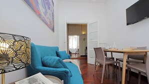 Un salon moderne avec un canapé bleu, une table à manger avec des chaises et un téléviseur à écran plat fixé au mur.