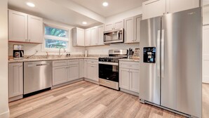 A modern kitchen with stainless steel appliances, white cabinetry, and a herringbone wood floor.