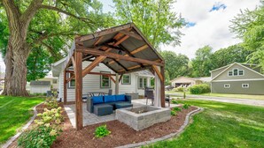 A covered outdoor seating area with a wooden pergola, a built-in bench, and a fire pit.