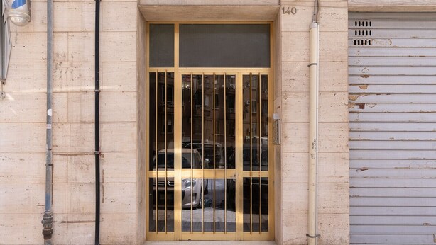 A building entrance with a metal gate, a number '140' above the door, and a closed garage door to the right. - Russu Suli Apartment 1 by Wonderful Italy (Siracusa)