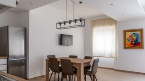 A modern kitchen with a stainless steel refrigerator, a dining table with six chairs, a flat-screen TV mounted on the wall, and a window with sheer curtains. - Russu Suli Apartment 1 by Wonderful Italy (Siracusa)