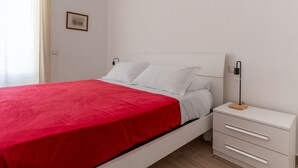 A single-bed room with a red bedspread, white bedding, a bedside table with drawers, a lamp, and a framed picture on the wall. - Russu Suli Apartment 1 by Wonderful Italy (Siracusa)