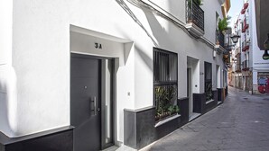 A narrow street with a white building featuring a black door and a balcony with plants. - Genteel Home Lagar II (Seville)