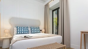 A neatly arranged bedroom with a bed, bedside tables, a bench, and a view through a window with curtains. - Genteel Home Lagar II (Seville)