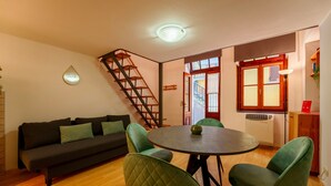 Uma sala de estar acolhedora com um sofá, cadeiras verdes, uma mesa redonda, uma escada e uma janela com vista.