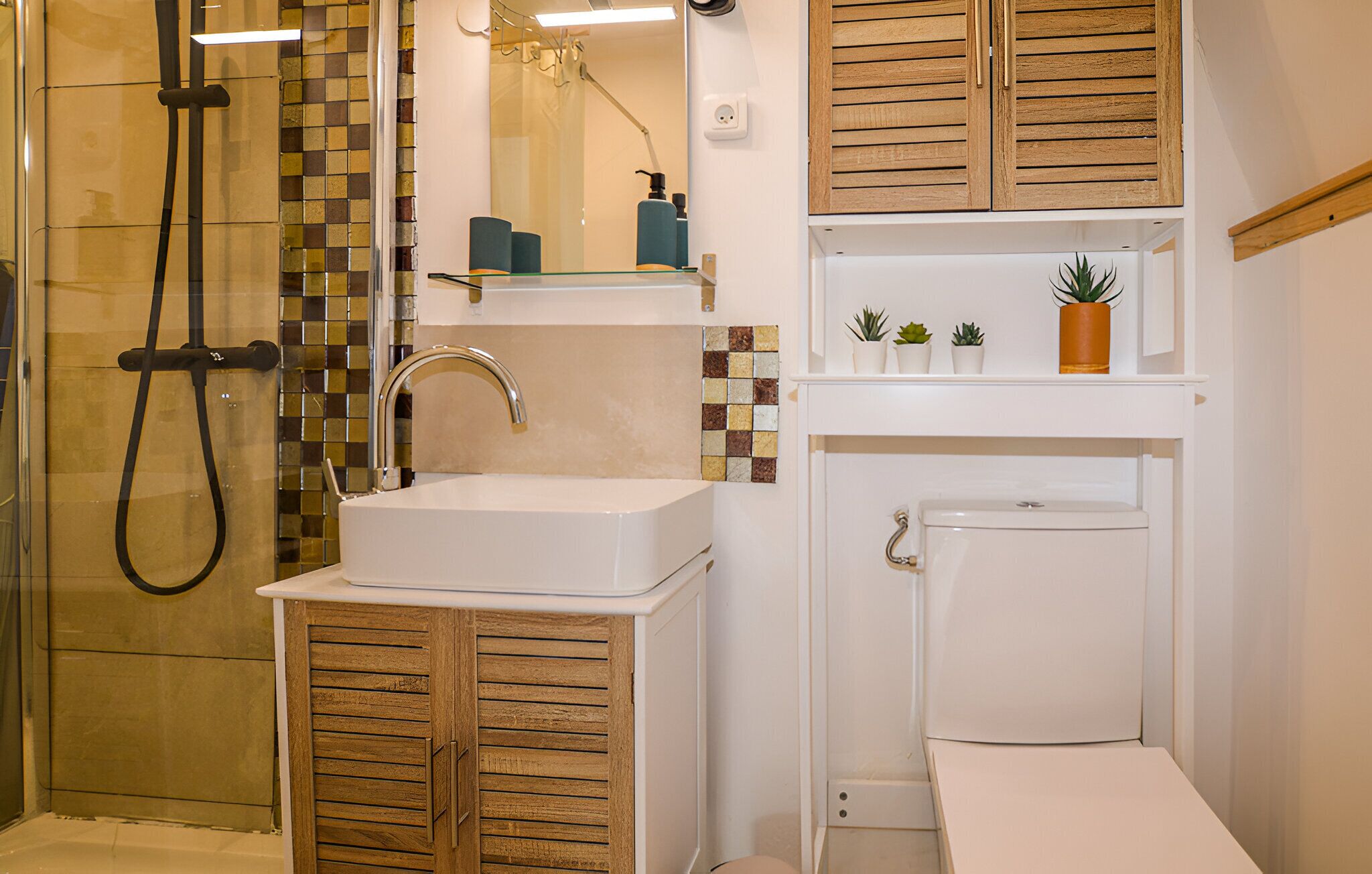 Un baño con cabina de ducha de vidrio, lavamanos blanco con grifo cromado, armarios de madera y un inodoro.