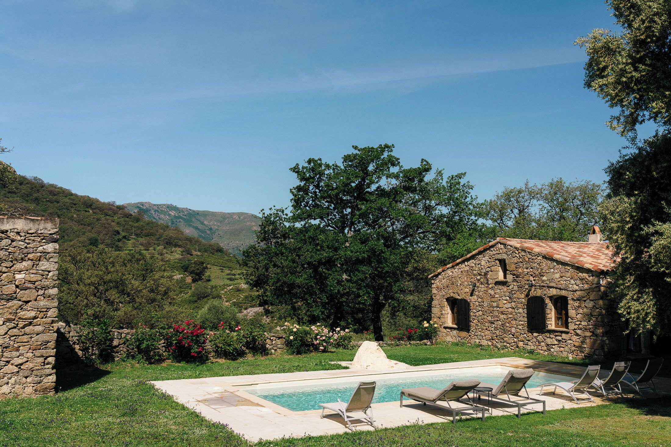 Un bâtiment en pierre doté d’une piscine et de chaises longues.