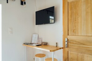 A room with a wooden desk, a mounted TV, a door, and a light switch.