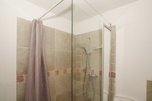 A glass-enclosed shower with a showerhead and handheld shower attachment.