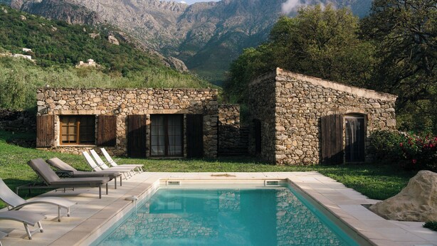 Una villa de piedra con piscina, rodeada de montañas y vegetación.