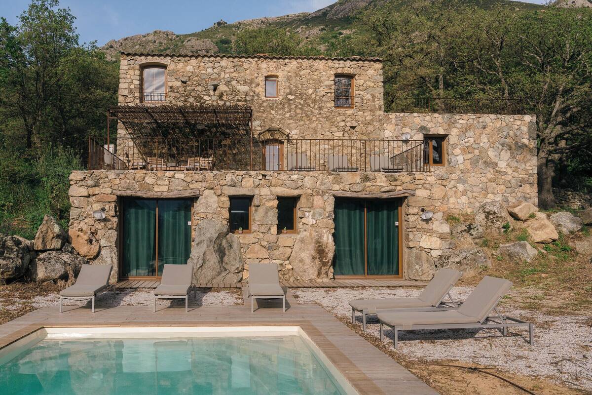 A stone villa with a pool, outdoor seating, and a mountainous backdrop.