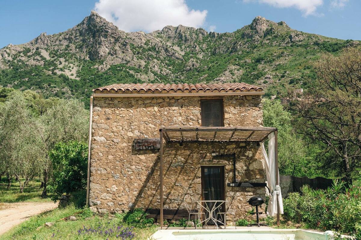 A stone building with a tiled roof, a small porch, and a view of a mountainous landscape.