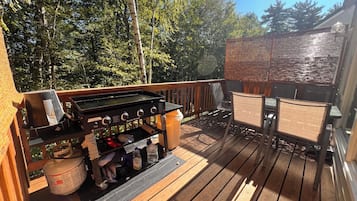 A wooden deck with a grill, chairs, and a table.