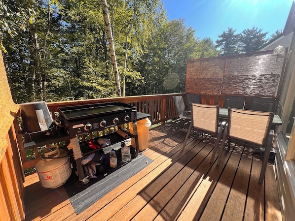 Una terraza de madera con una parrilla, sillas y una mesa.