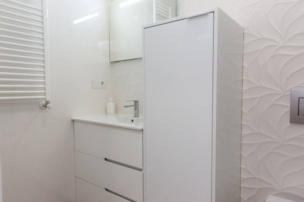 A bathroom with a white cabinet, a sink, and a mirror.