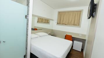 Habitación de hotel con cama, escritorio, silla, refrigerador pequeño y televisor montado en la pared.