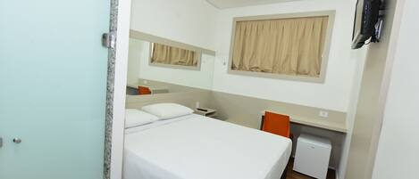 Une chambre d’hôtel équipée d’un lit, d’un bureau, d’une chaise, d’un petit réfrigérateur et d’un téléviseur fixé au mur.