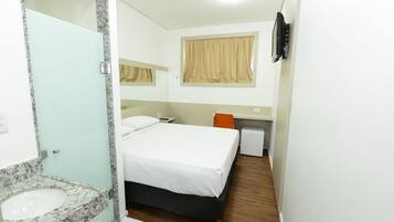 Habitación de hotel con cama, un escritorio pequeño, un espejo, ventana con cortinas y un lavamanos.