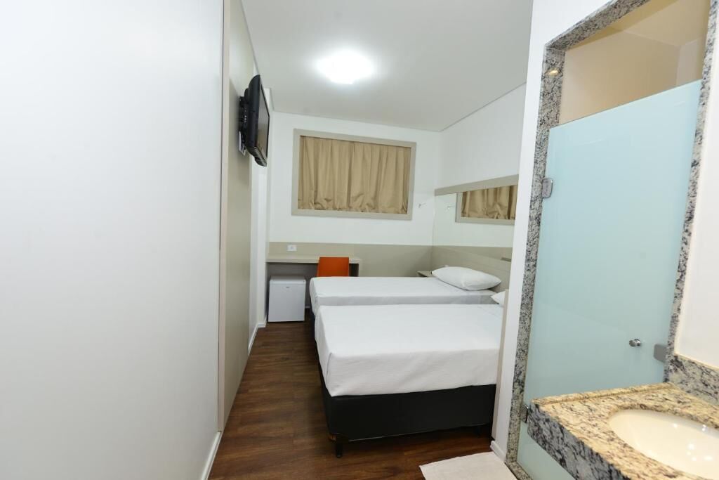 A bedroom with two beds, a desk, a television, and a bathroom with a granite sink.