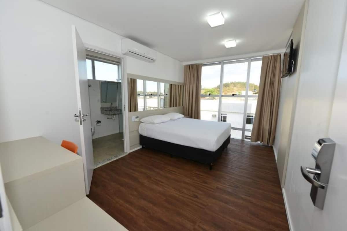 A hotel room with a bed, a desk, and a view through the window.