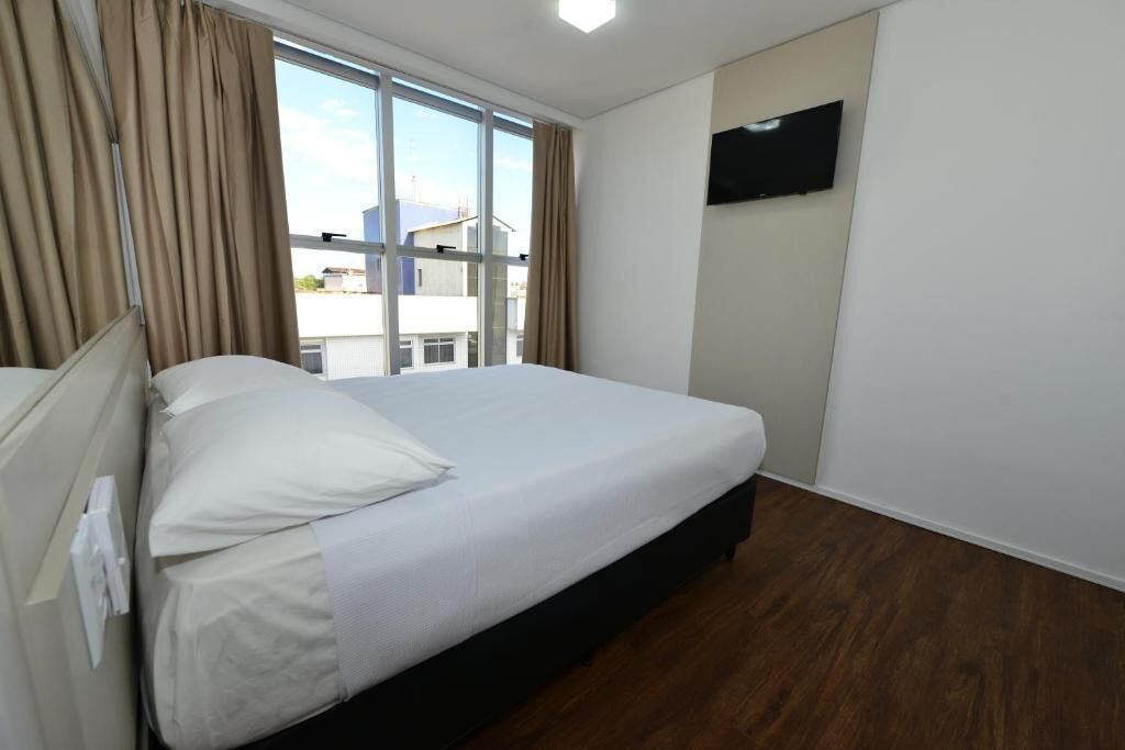 Habitación de hotel con una cama grande, un televisor de pantalla plana montado en la pared y una ventana con cortinas.