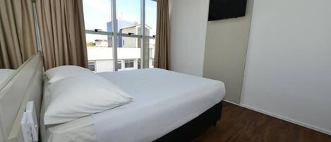 Habitación de hotel con una cama grande, un televisor de pantalla plana montado en la pared y una ventana con cortinas.