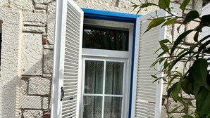 A stone wall with a window featuring white shutters and a blue frame.