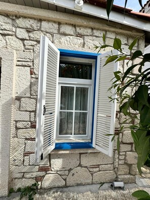 Una pared de piedra con una ventana, contraventanas blancas y marco azul.