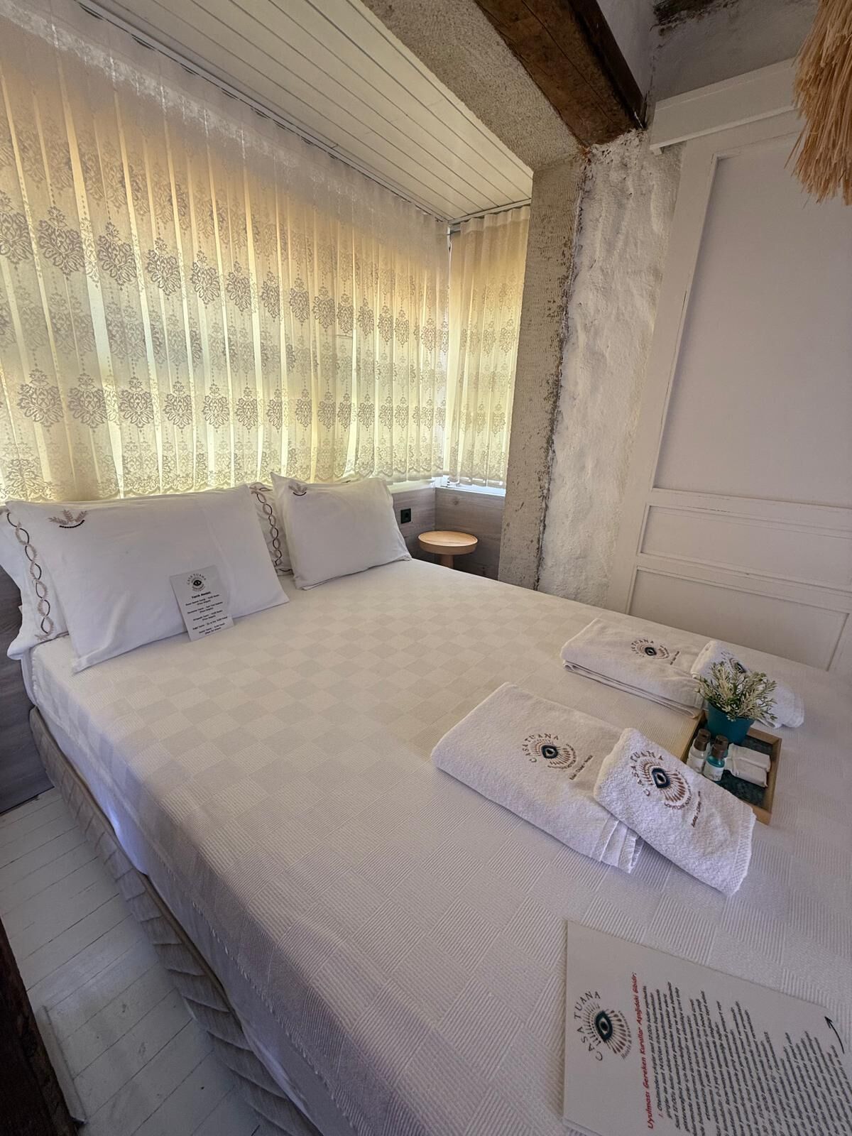 Une chambre d’hôtel avec un lit, des oreillers, une petite table ronde et une fenêtre avec des rideaux.