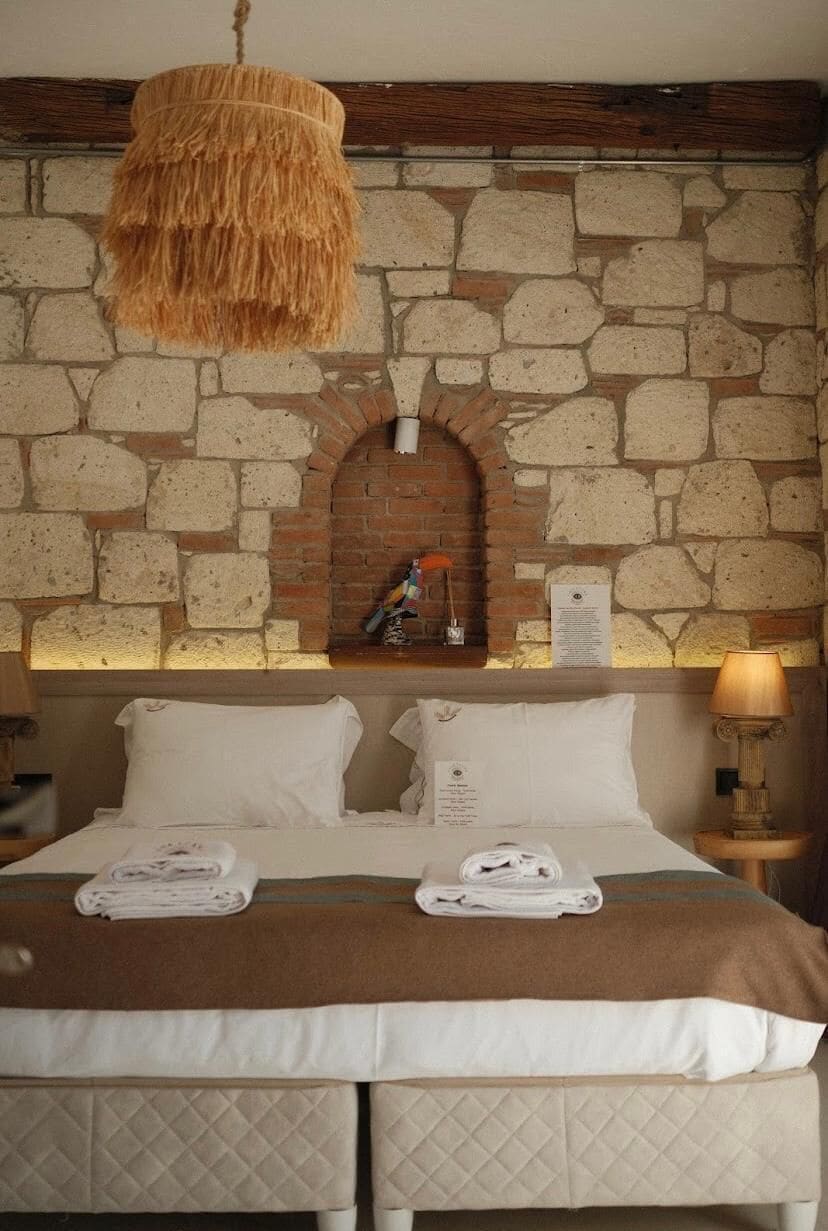 A hotel room with a stone wall, a bed with white linens, and a hanging light fixture.