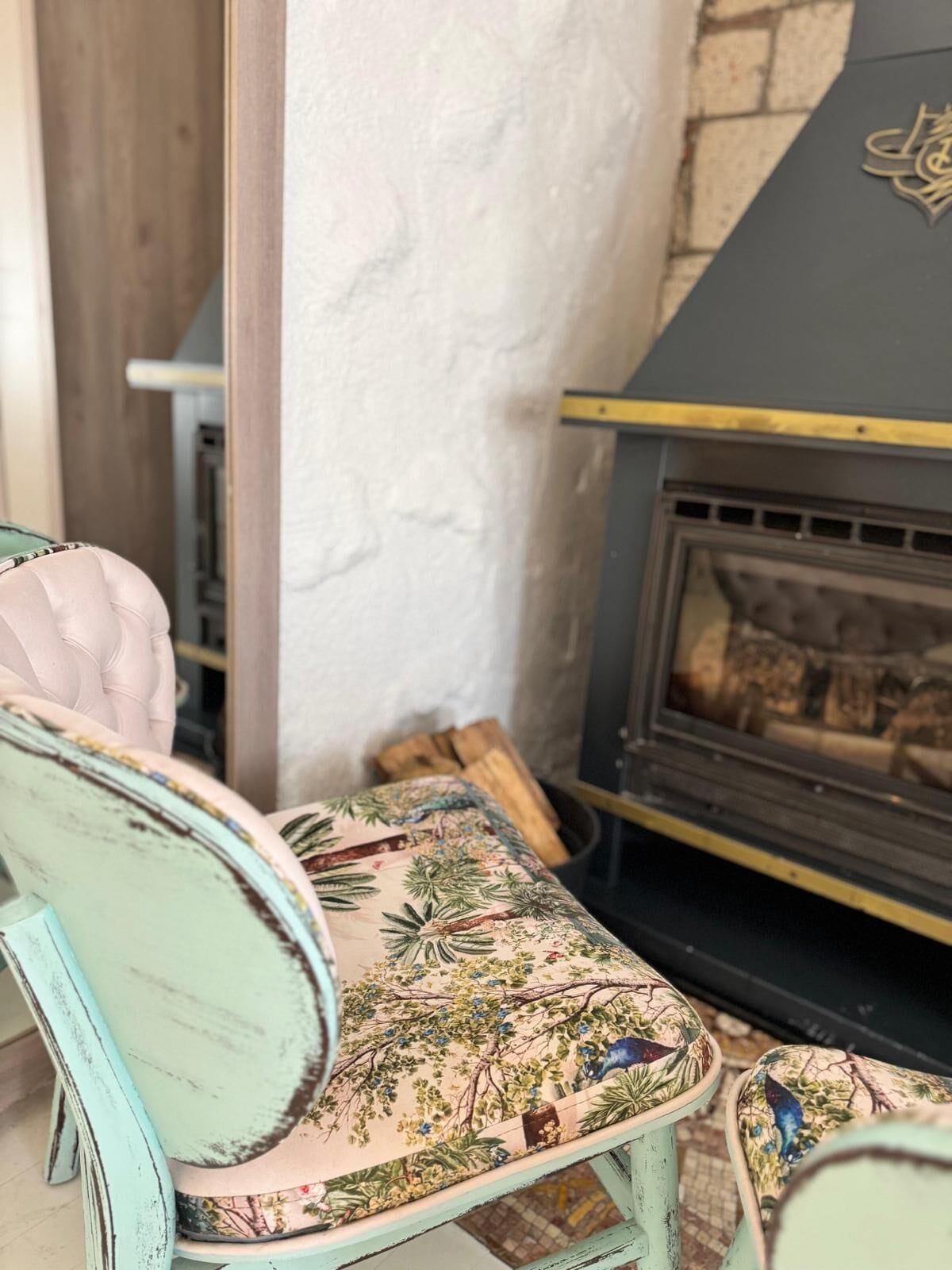 A vintage-style chair with floral upholstery next to a fireplace with a stone wall backdrop.