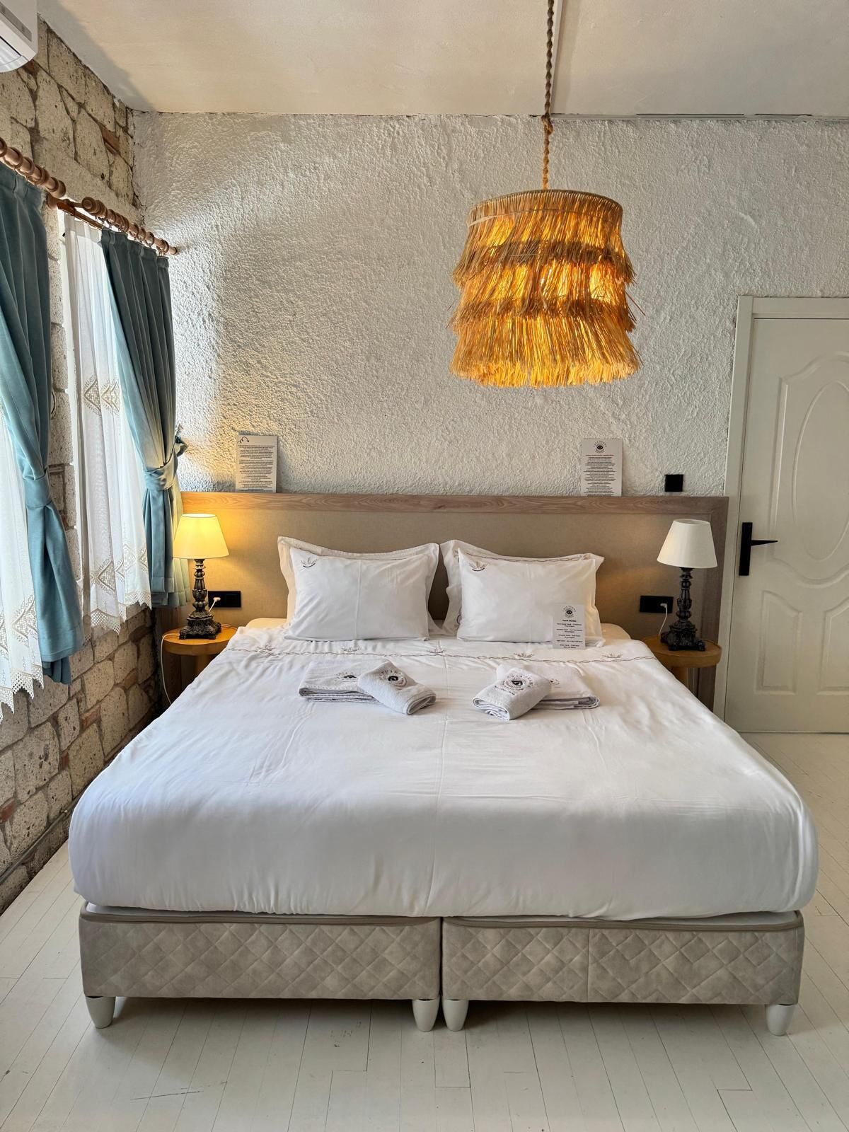 A hotel room with a large bed, two bedside tables with lamps, a textured wall, and a hanging light fixture.