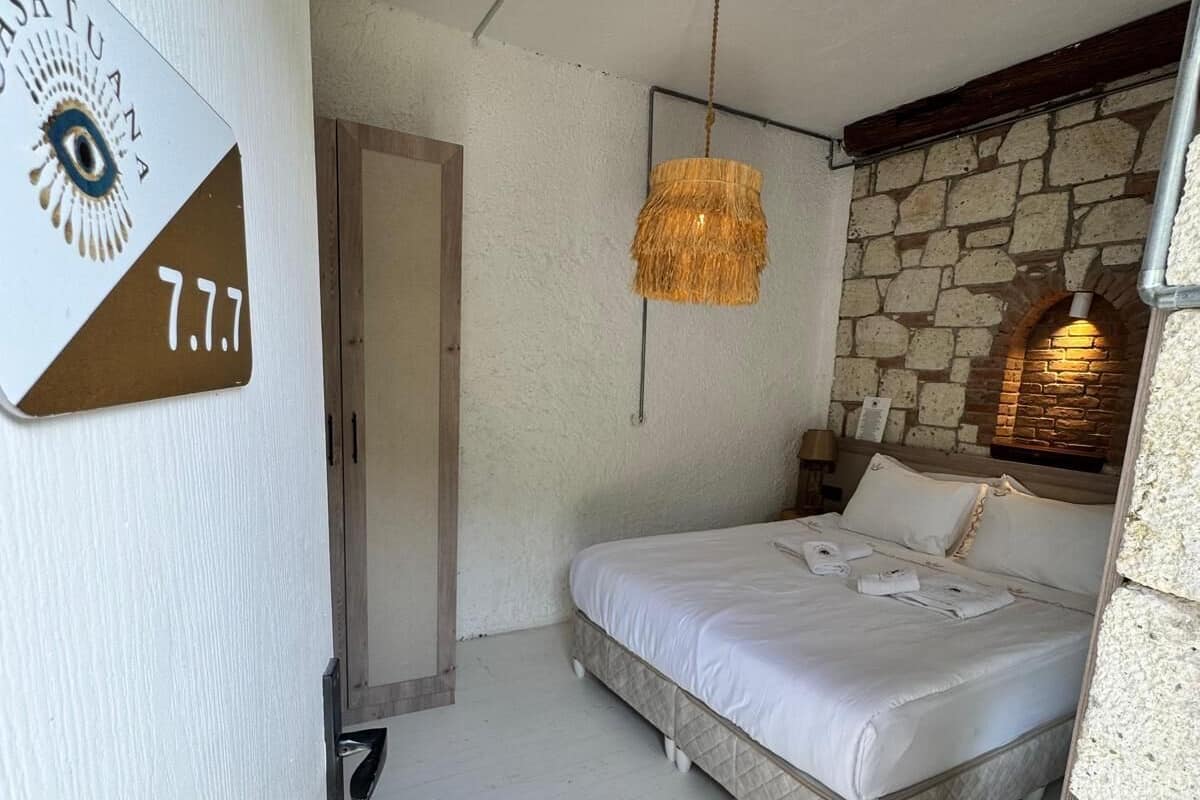 A bedroom with a bed, a hanging light fixture, a stone wall, and a door.