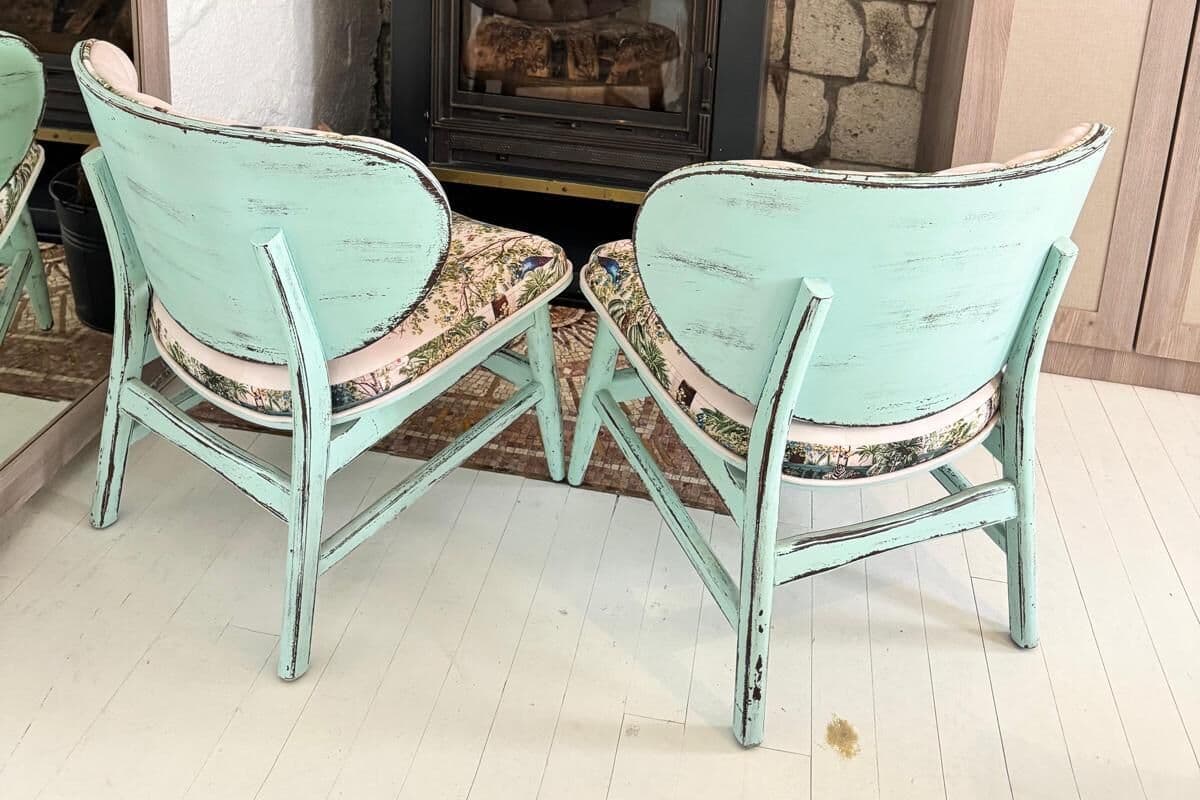A stone wall with a fireplace, two turquoise chairs, and a wooden cabinet.