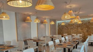 A restaurant with multiple dining tables and chairs, overhead lighting, and a stone wall in the background. - Casa Sophie Albufeira Apartment With 2 Bedrooms (Albufeira)