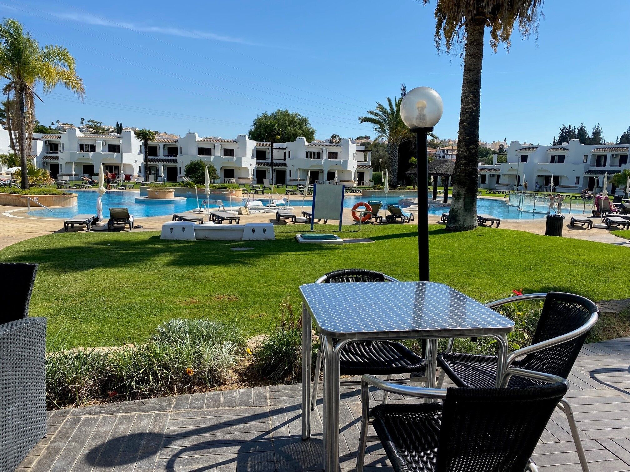 A pool area with lounge chairs and a table, surrounded by a well-maintained lawn and palm trees.