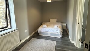 Une chambre à coucher moderne avec un grand lit, une fenêtre, un radiateur, une moquette et une porte.