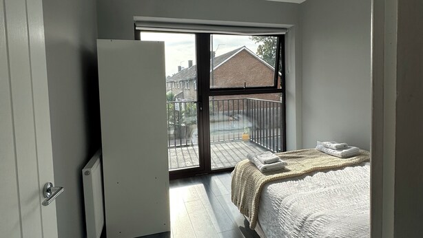 Une chambre avec une grande fenêtre, un lit, un radiateur et une porte.