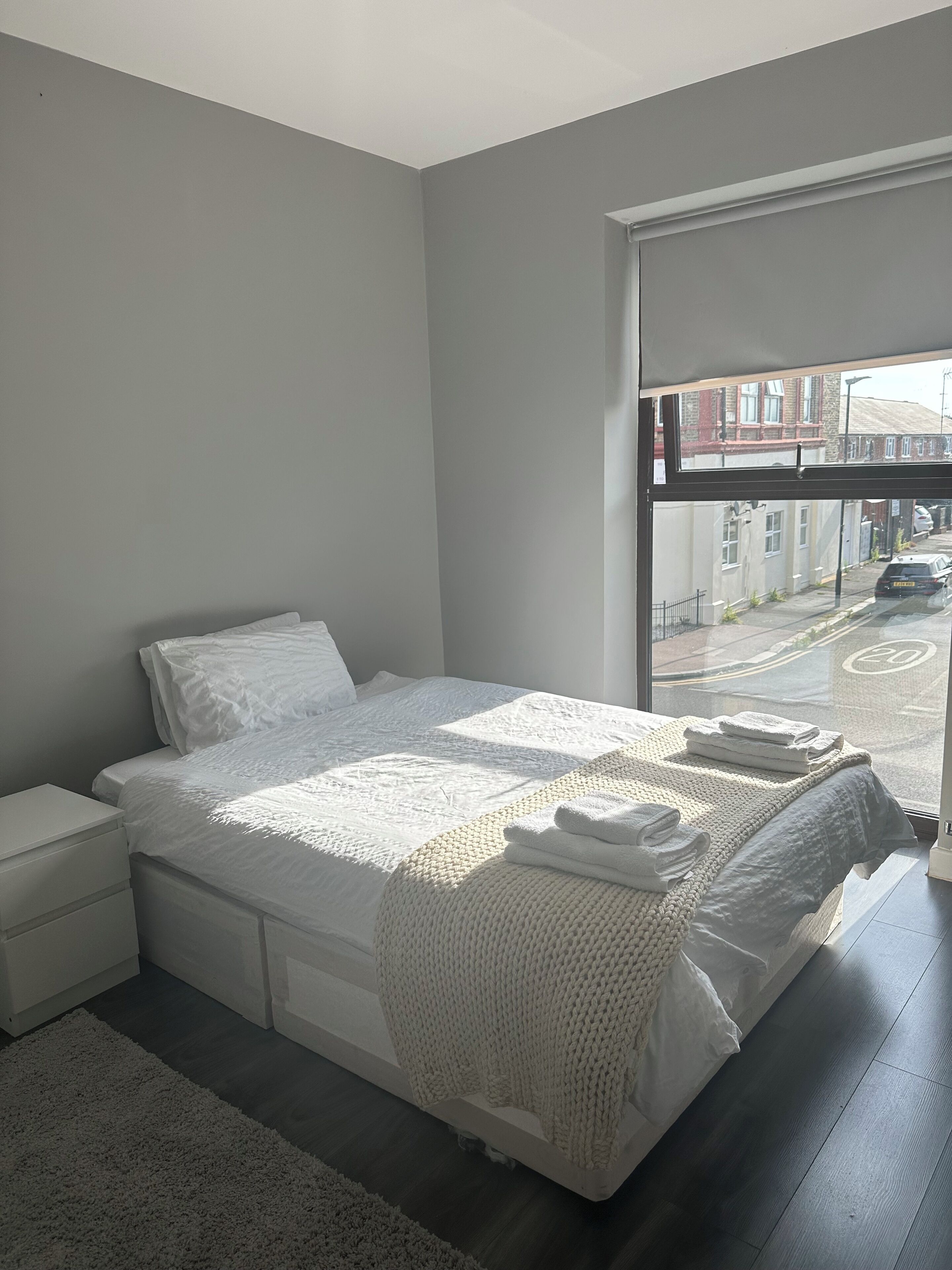 A bedroom with a large bed, a nightstand, a window with a view of a street.