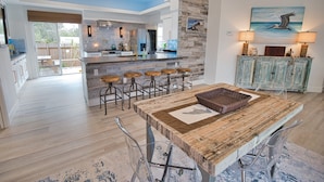 A modern kitchen with a central island, bar stools, and a dining table with a basket. - The Windsor @ Englewood Beach (Englewood)