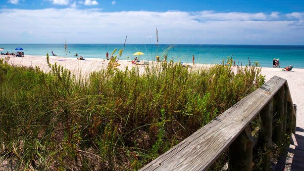 A beach with a wooden boardwalk, clear blue sky, and calm sea. - The Windsor @ Englewood Beach (Englewood)