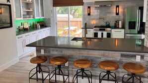 A modern kitchen with a central island, bar stools, a stove, and a refrigerator. - The Windsor @ Englewood Beach (Englewood)