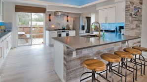 A modern kitchen with a large island, bar stools, and a view to the backyard. - The Windsor @ Englewood Beach (Englewood)