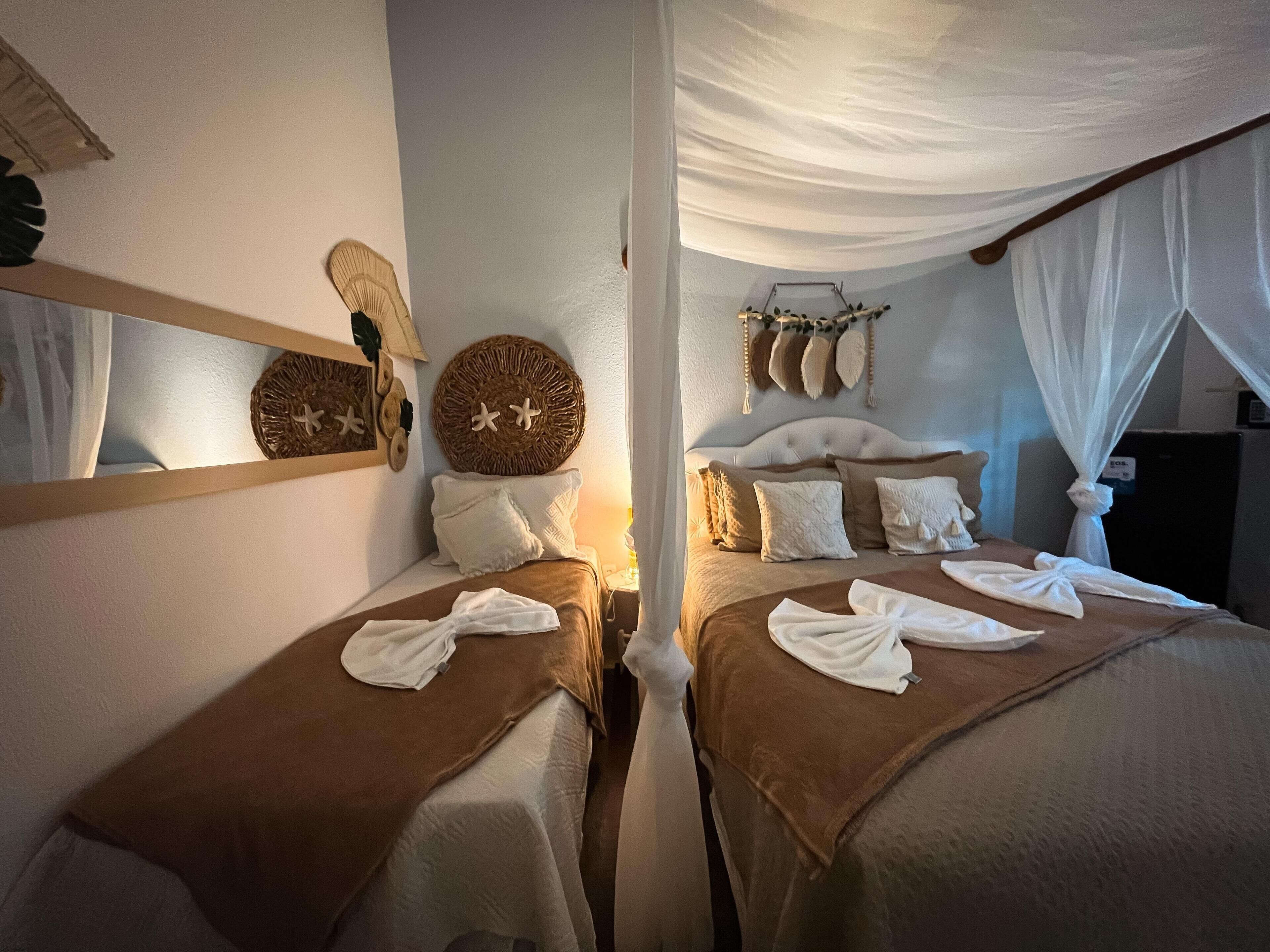 A room with two beds, each with a brown bedspread and white pillows. There are decorative wall hangings above the beds, including a woven circular piece and a wall-mounted item with feathers.